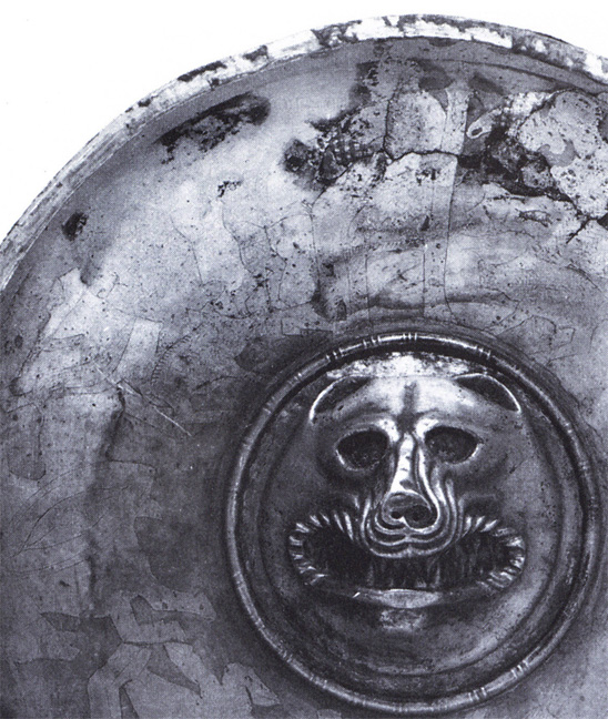 section of silver plate with wolf head protruding from center, and inlaid metal design around rim